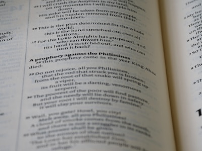 An open book with visible text on its pages, featuring several sentences in a serif typeface. The text contains a title in bold, indicating a prophecy against the Philistines, followed by numbered verses that appear to be from a biblical or religious context. The page edges are slightly curved, emphasizing the book's thickness and texture.