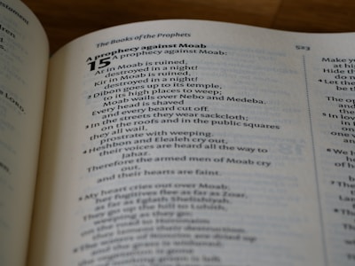 A close-up view of a book open to a page with text from 'The Books of the Prophets.' The passage is titled 'A prophecy against Moab,' with chapter and verse numbers marking the start and progression of the text. The text is printed in a serif font, and the page is well lit, indicating a reading environment.