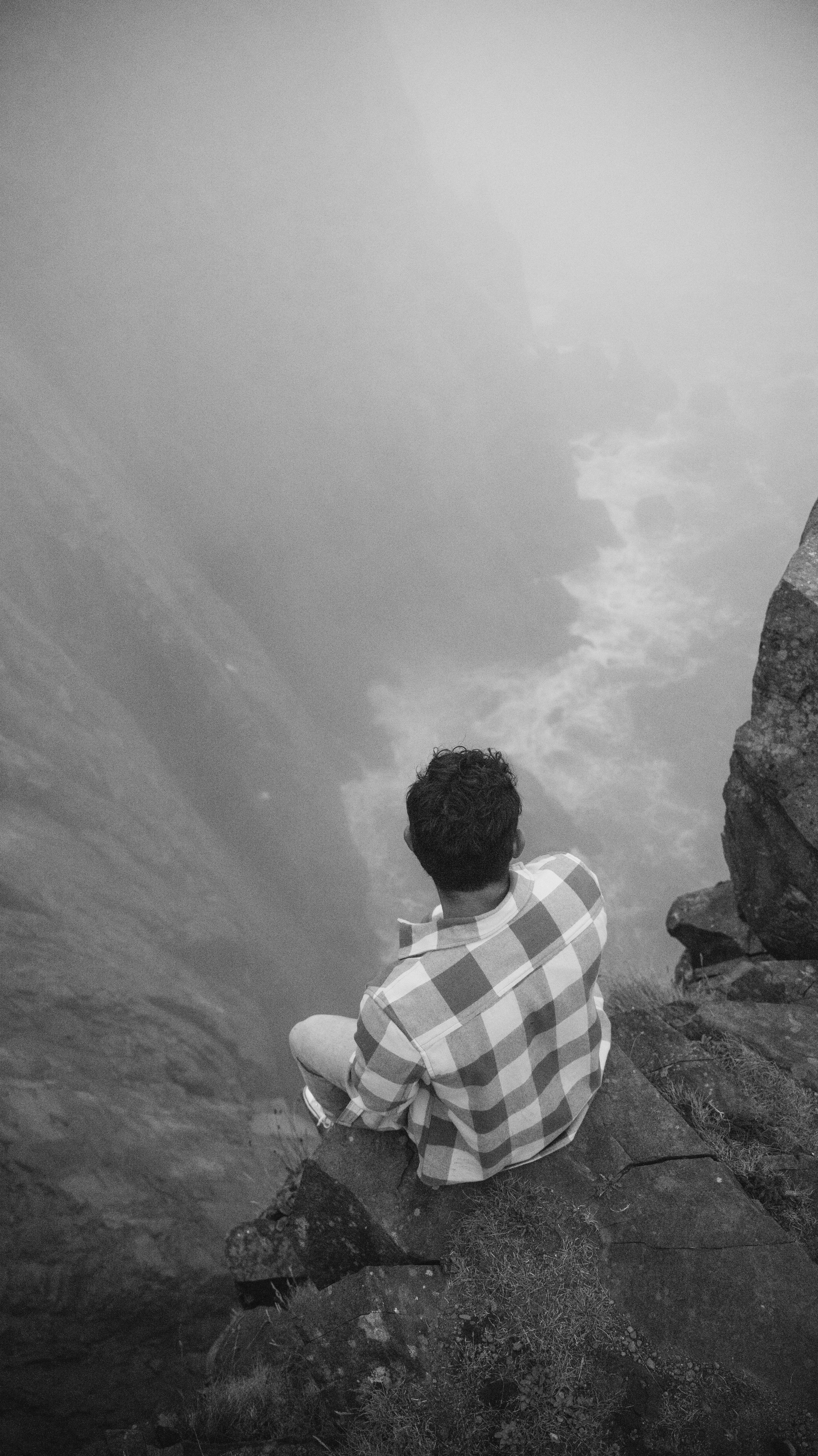 a man sitting on top of a rock next to a body of water