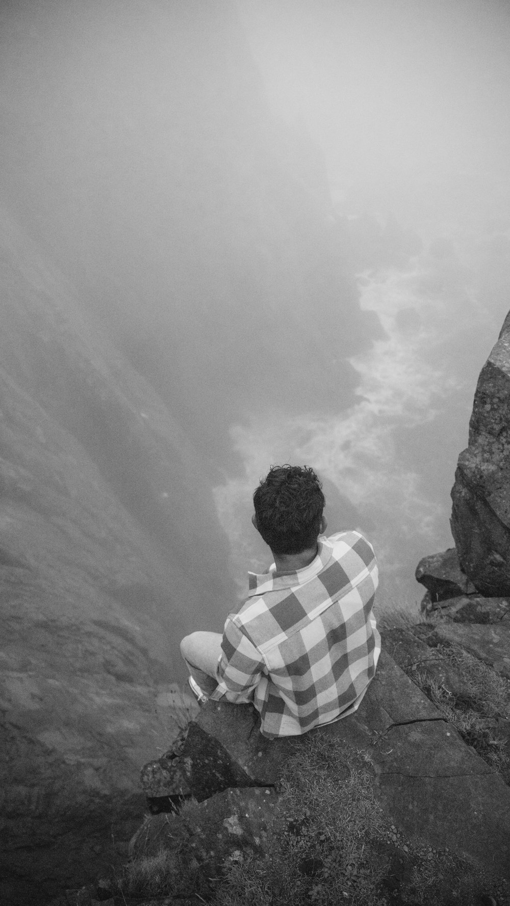 Un hombre sentado en la cima de una roca junto a un cuerpo de agua