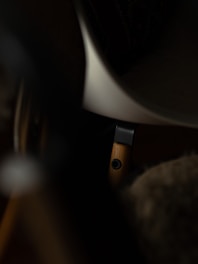 The image depicts a close-up view of a wooden furniture leg, partially visible, with a dark metal bracket attached. The background is in shadows, giving a dim and mysterious atmosphere.