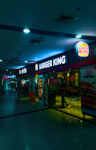 A bustling Burger King outlet with customers enjoying meals inside a modern Delhi shopping complex.