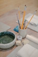 a wooden table topped with a bowl of paint and brushes