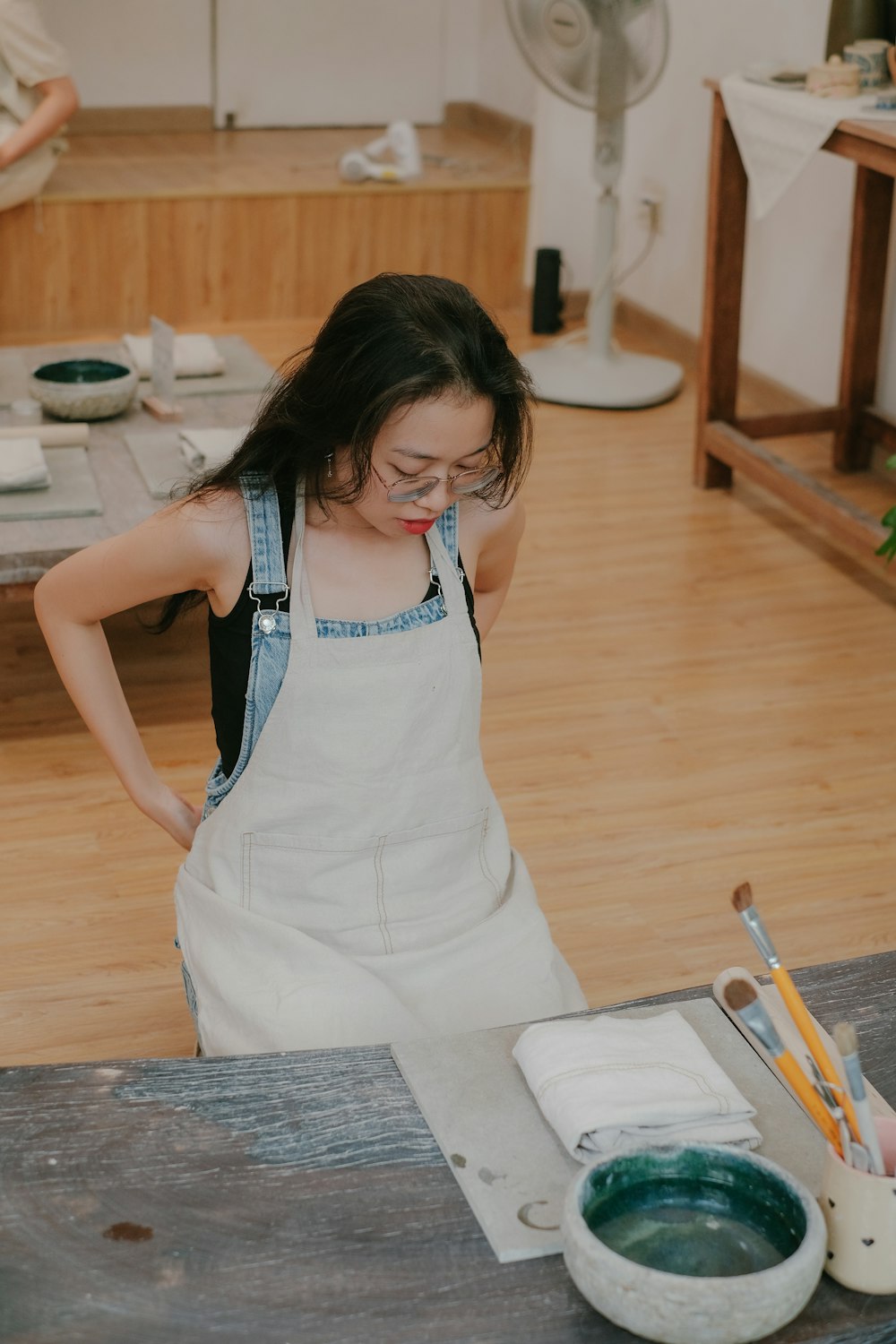 a woman in a white apron painting on a piece of wood