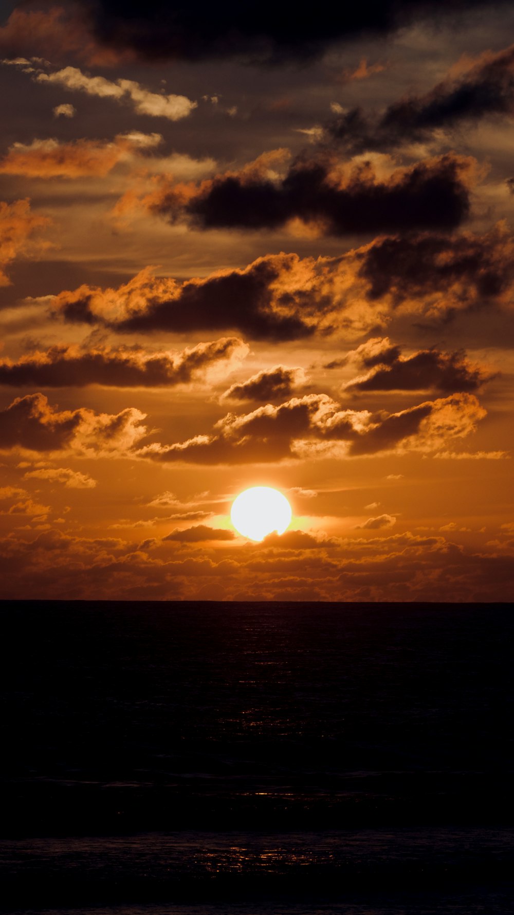 the sun is setting over the ocean on a cloudy day