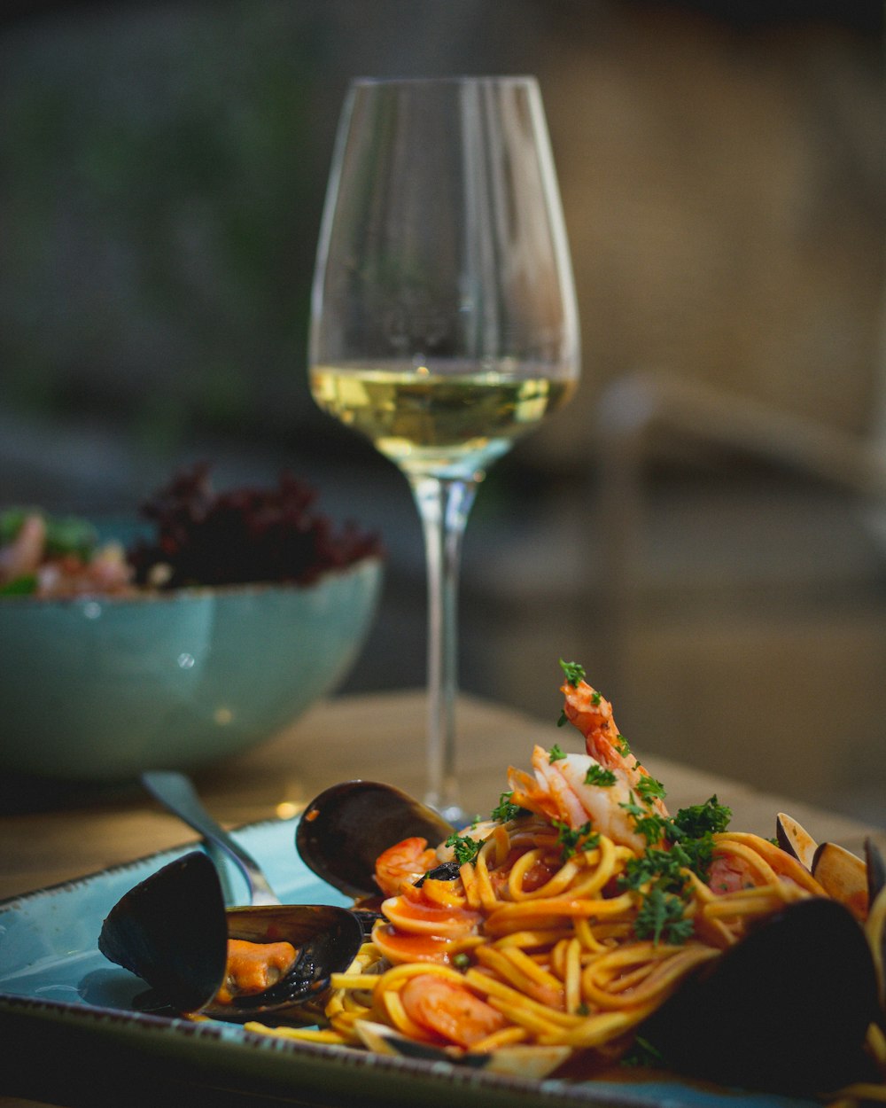 a plate of pasta with shrimp and mussels next to a glass of wine