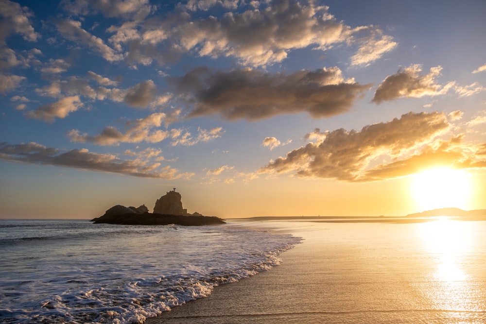 the sun is setting over the ocean with a small island in the distance