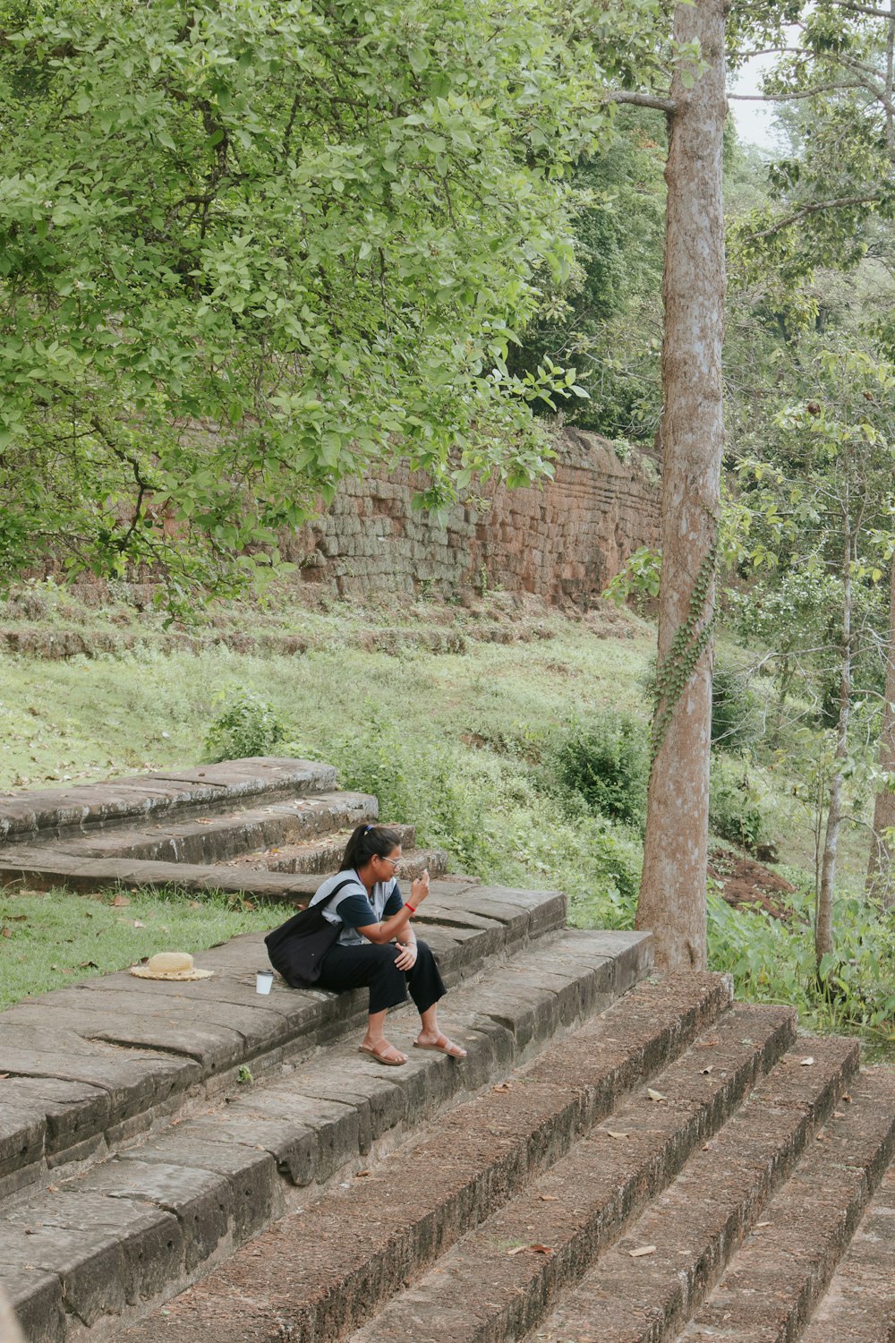 a woman sitting on a stone step next to a tree
