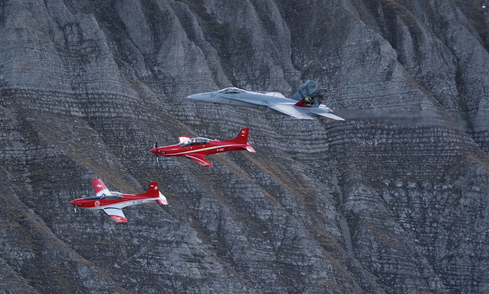three red and white planes flying over a mountain