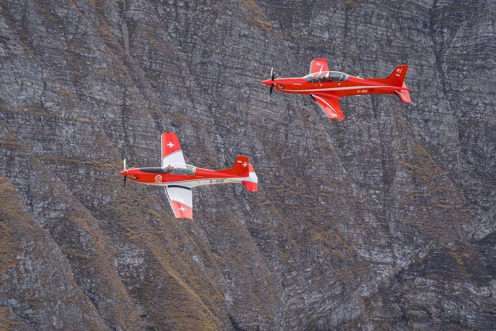two red and white planes flying over a mountain
