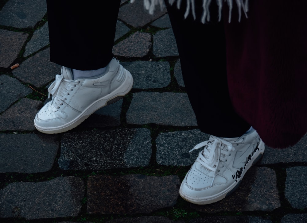 a person standing on a cobblestone walkway wearing white sneakers