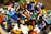 A collection of colorful plastic toy figures scattered in disarray. Various figures are dressed in different outfits, representing a diverse array of themes and professions. The toys are made of bright plastic, with some figures facing upwards and others sideways or upside down. The scene appears playful and chaotic.