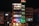 A multi-story hotel building is lit up at night with various colored lights. The facade displays the hotel name 'SDM Vedanta' and the sign '24x7 Restaurant' at the top. The building features a modern design with glass windows and a combination of warm and cool lighting. Adjacent structures are partially visible.