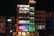 A multi-story hotel building is lit up at night with various colored lights. The facade displays the hotel name 'SDM Vedanta' and the sign '24x7 Restaurant' at the top. The building features a modern design with glass windows and a combination of warm and cool lighting. Adjacent structures are partially visible.