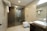 A modern bathroom features a glass-enclosed shower area with a mounted showerhead. A white ceramic sink rests on a dark wooden counter, alongside a mirror and toiletries. Towels hang on a rack above the commode, and the space is illuminated by ceiling lights.