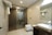 A modern bathroom features a glass-enclosed shower area with a mounted showerhead. A white ceramic sink rests on a dark wooden counter, alongside a mirror and toiletries. Towels hang on a rack above the commode, and the space is illuminated by ceiling lights.