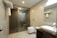 A modern bathroom features a glass-enclosed shower area with a mounted showerhead. A white ceramic sink rests on a dark wooden counter, alongside a mirror and toiletries. Towels hang on a rack above the commode, and the space is illuminated by ceiling lights.