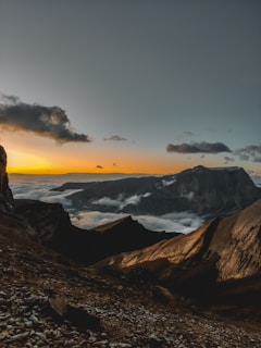 A dramatic landscape shot of rugged mountains under a cloudy sky at dusk.