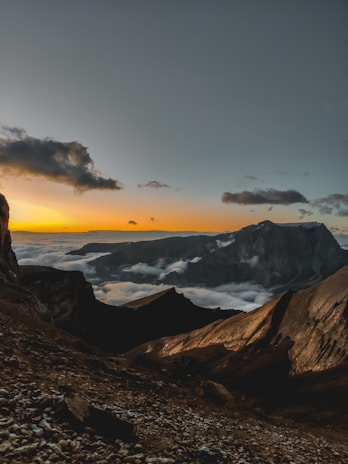 A dramatic landscape shot of rugged mountains under a cloudy sky at dusk.