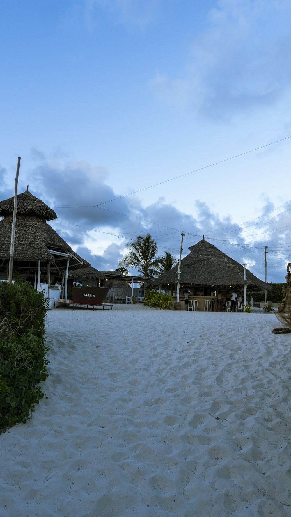 a sandy path leading to a beach with thatched huts