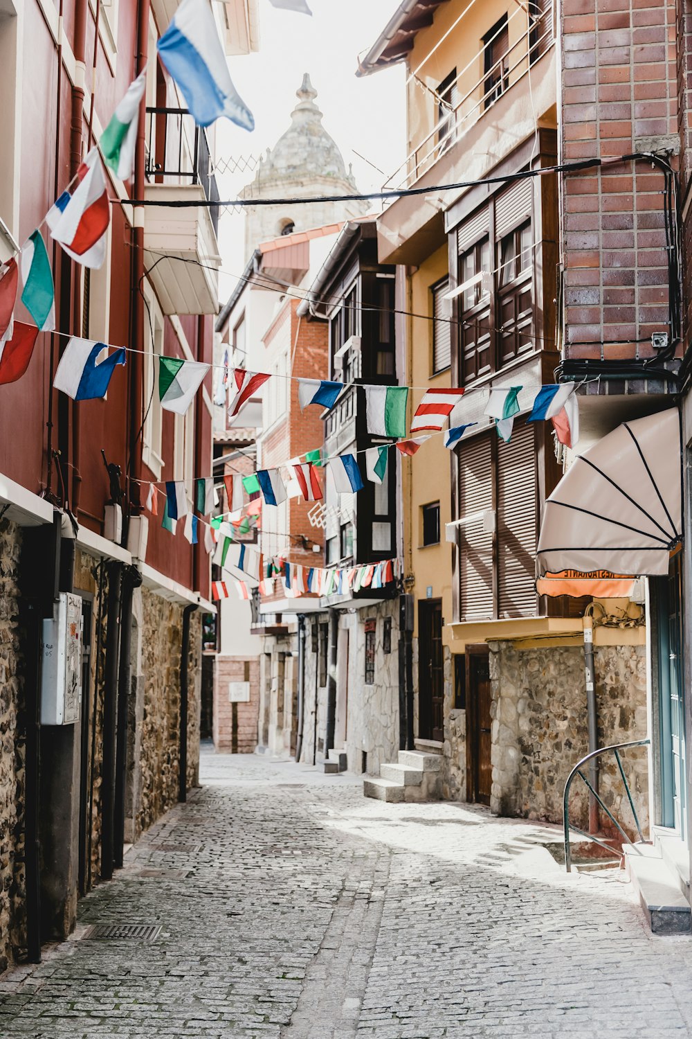 a cobblestone street lined with buildings and flags