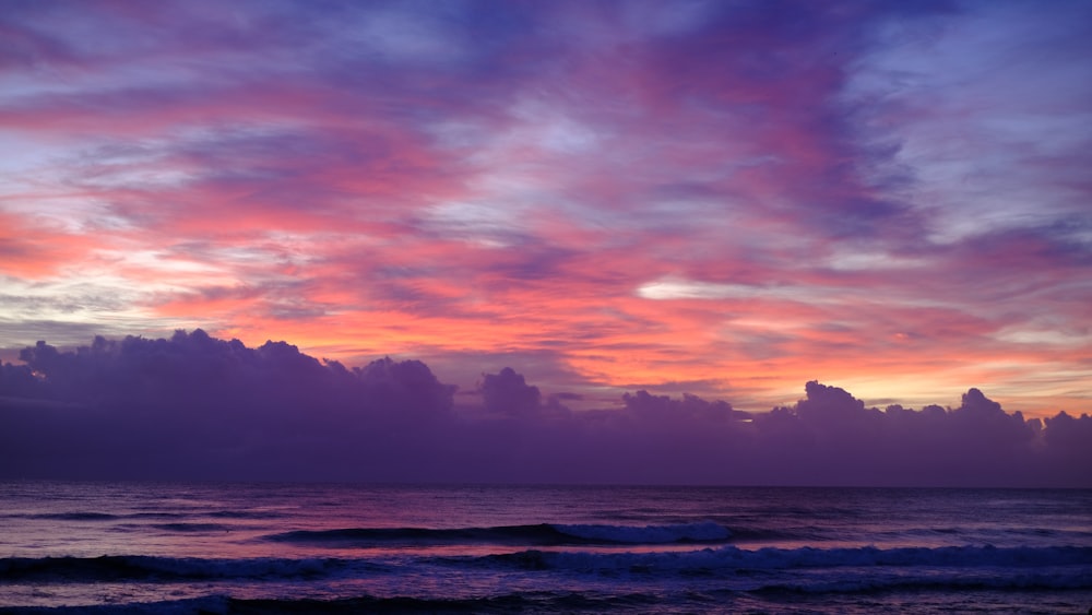 a sunset over the ocean with clouds and waves