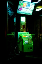 a green payphone sitting in a dark room