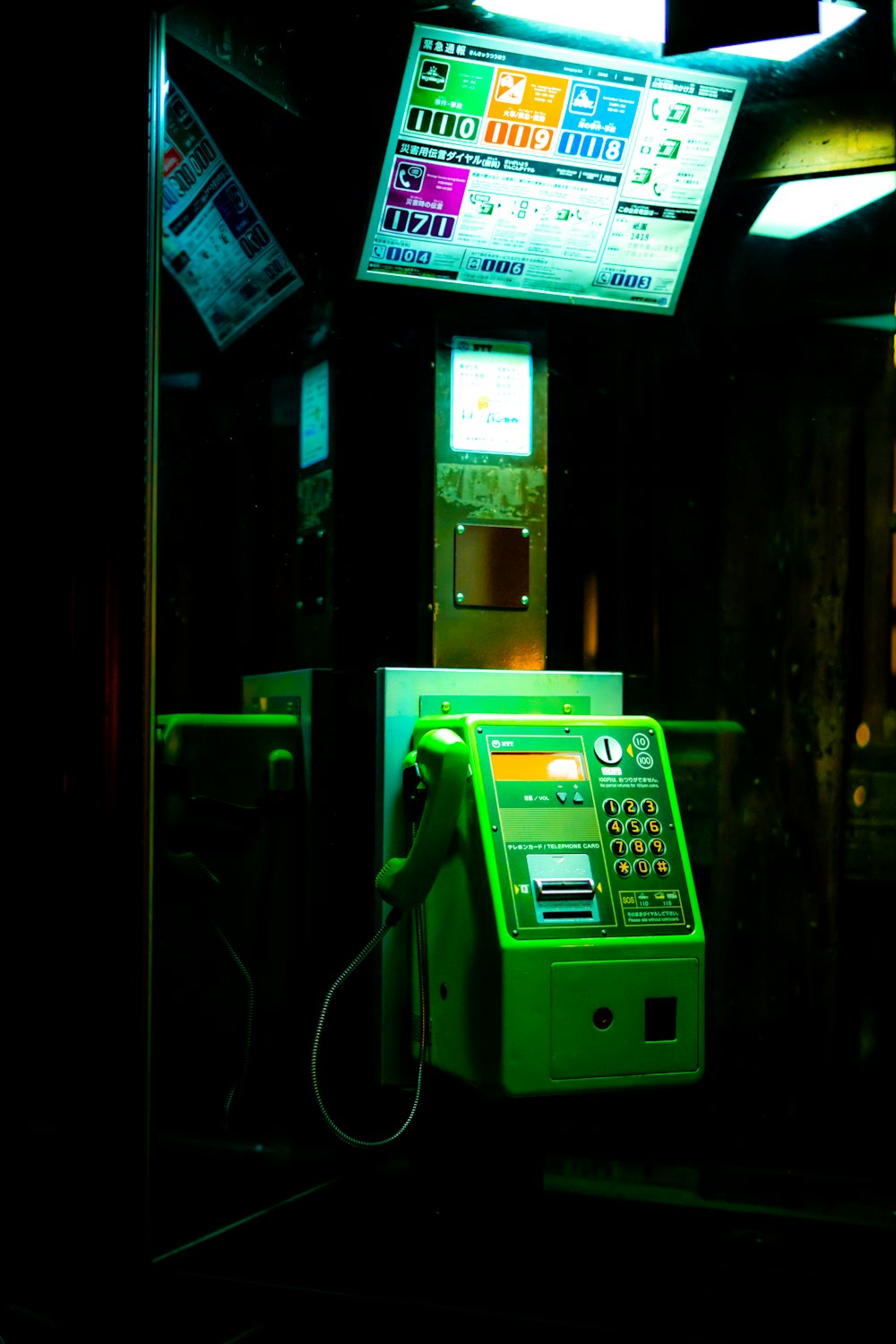 a green payphone sitting in a dark room