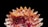 A digitally created flower with layered petals displayed against a black background. The petals vary in shades of orange, pink, and white, creating a vibrant and intricate pattern.