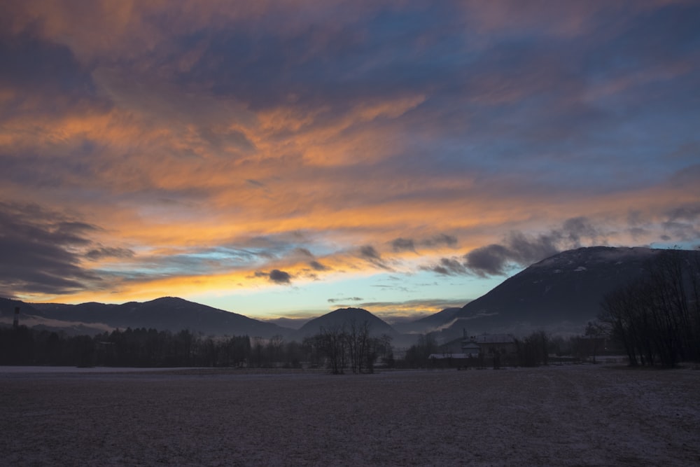 a field with mountains in the background at sunset