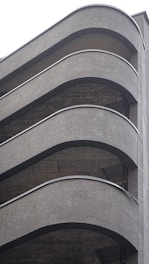 A multistory parking structure with curved, modernist architectural elements featuring smooth, gray concrete surfaces. The repetitive pattern of the floors and the gentle arcs of the railings lend a sense of sleek design to the building.