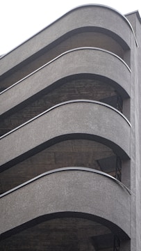 A multistory parking structure with curved, modernist architectural elements featuring smooth, gray concrete surfaces. The repetitive pattern of the floors and the gentle arcs of the railings lend a sense of sleek design to the building.