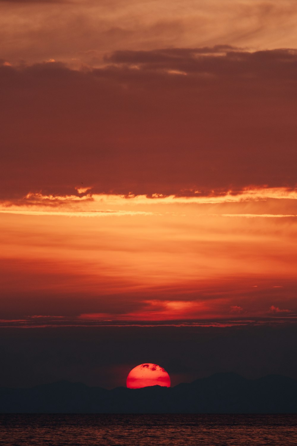 the sun is setting over the ocean with mountains in the background