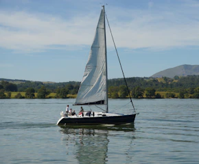 Participants enjoying a serene sailing trip along a lush green coastline under clear skies.