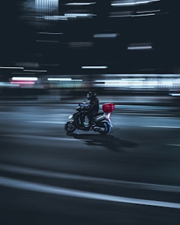 Delivery courier riding a motorbike at night with neon city lights in the background.
