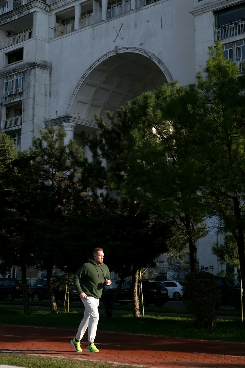 a man in a green sweatshirt is walking in front of a building