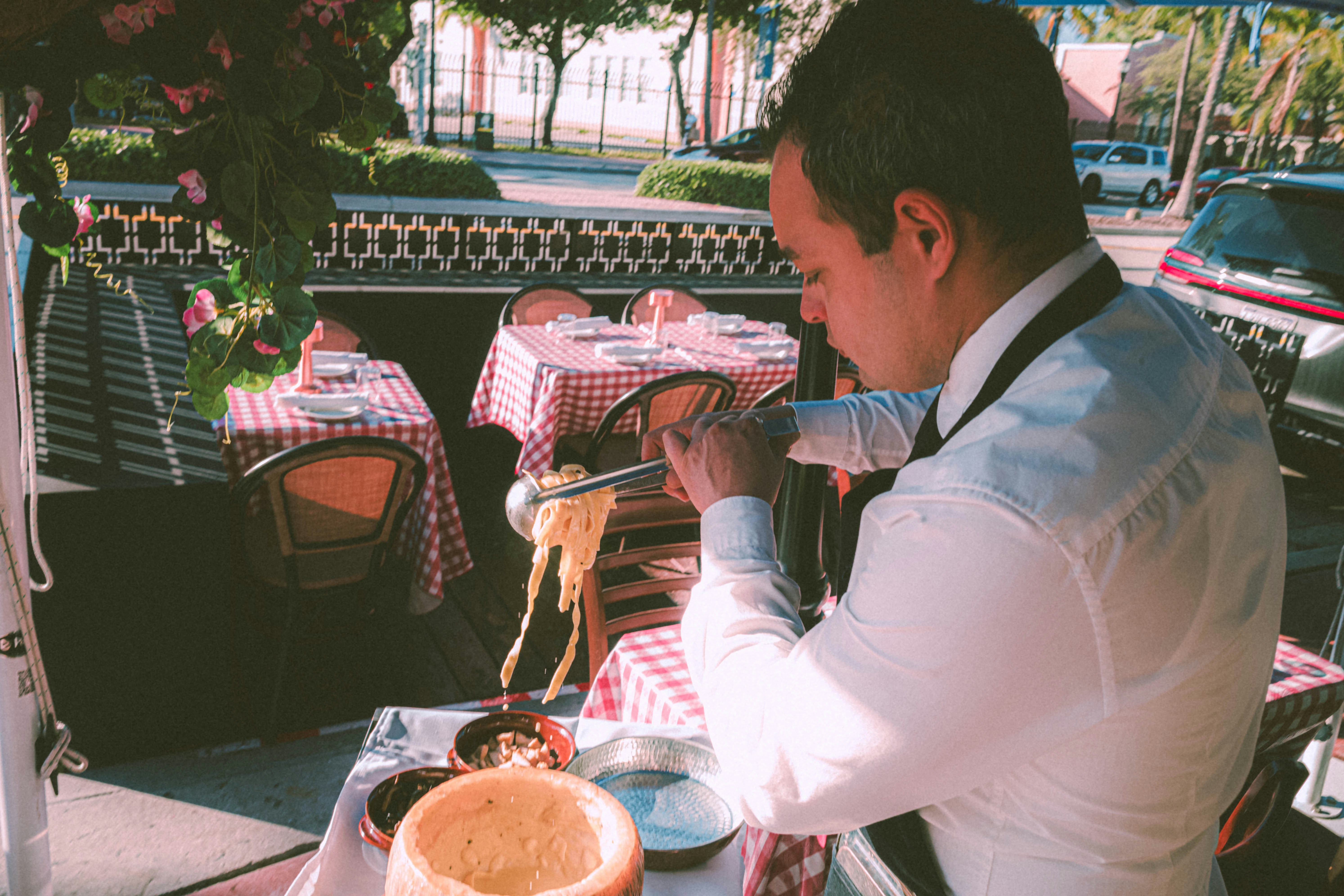 a man sitting in a table with a plate of food in front of him and a waiter serving pasta