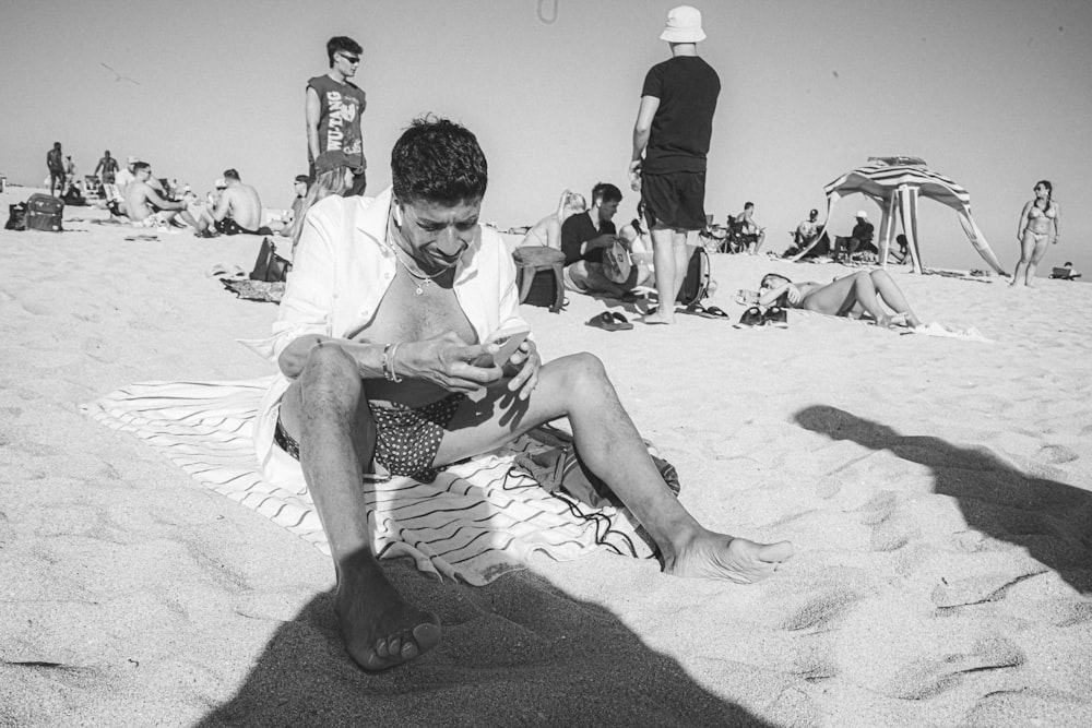 a man sitting on the beach looking at his cell phone