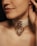 A close-up of a person's neck with a beige choker featuring a large metallic ring and a decorative pendant.