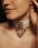 A close-up of a person's neck with a beige choker featuring a large metallic ring and a decorative pendant.