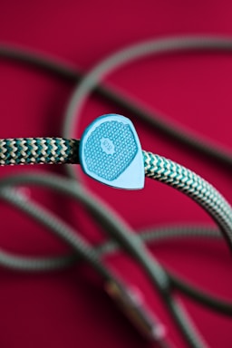 A braided rope with a zigzag pattern in shades of teal and white, accented by a plastic piece with intricate designs and the number 9.8. The background is a rich magenta, which contrasts with the color of the rope.