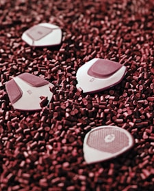 Several geometric objects with labels are scattered on a surface covered with small red cylindrical pellets. The objects appear to be white with maroon sections.