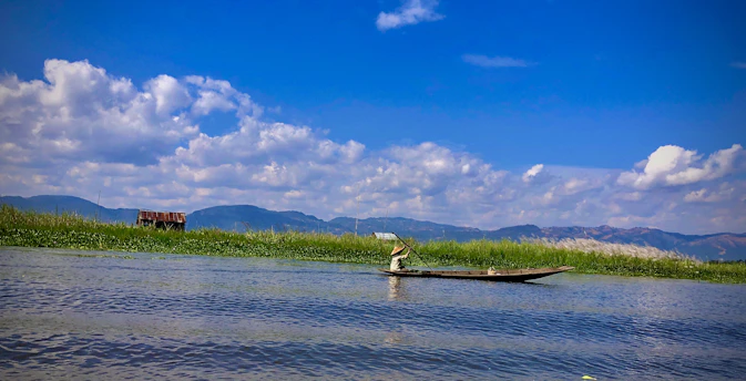 A serene lake at dawn with a lone fisherman casting his line, surrounded by misty mountains.