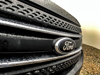 Close-up view of a Ford vehicle grille with water droplets on a dark surface, showcasing the Ford emblem prominently.