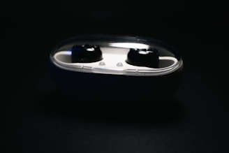 Black wireless earbuds nested in a white charging case with a transparent lid, set against a dark background.