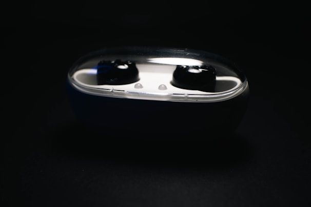 Black wireless earbuds nested in a white charging case with a transparent lid, set against a dark background.