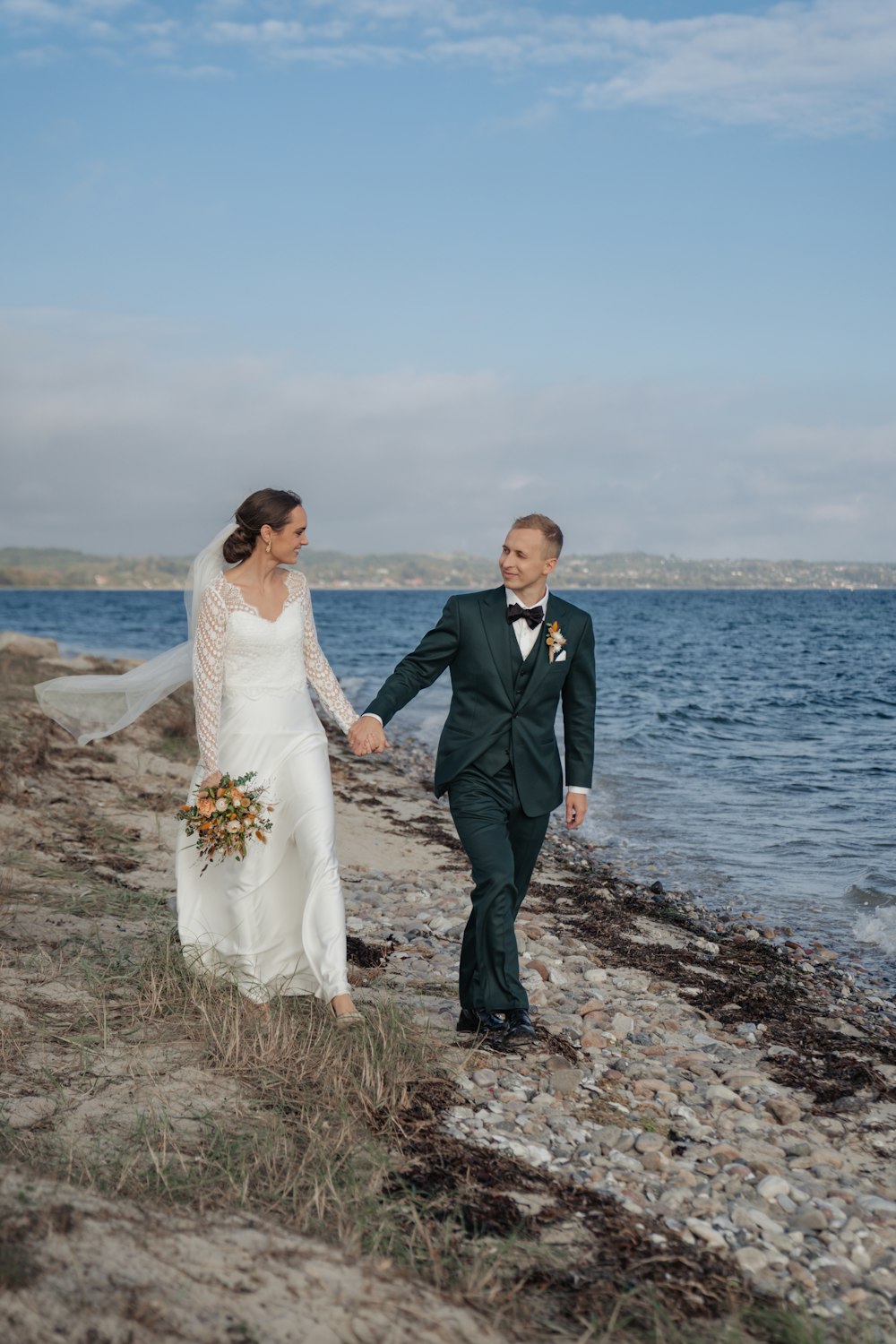 a bride and groom walking on the beach
