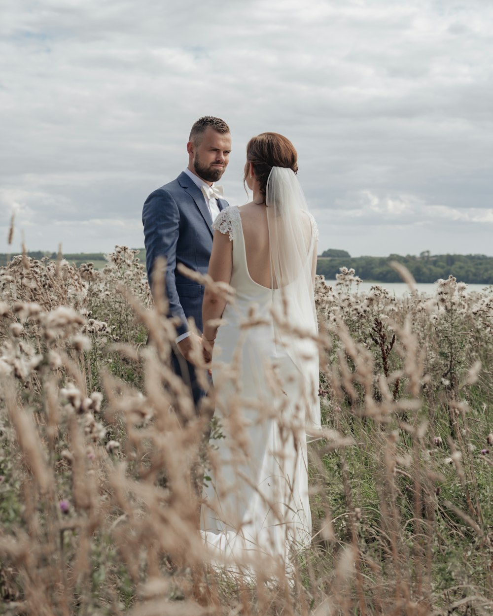 a bride and groom standing in a field of tall grass