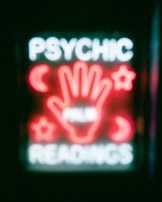 A neon sign featuring the words 'Psychic Readings' with a central image of a hand surrounded by symbols like crescent moons and stars.