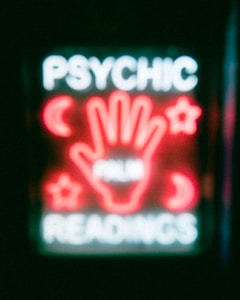 A neon sign featuring the words 'Psychic Readings' with a central image of a hand surrounded by symbols like crescent moons and stars.